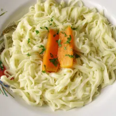 Stary przepis na makaron, podany z marchewką i natką pietruszki na talerzu ozdobionym kłosami zbóż i kwiatami.