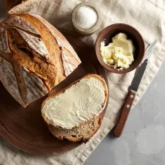 Domowy chleb pieczony w piekarniku, kromka z masłem, sól i nóż. Idealny przepis na śniadanie.