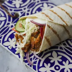 Pyszny kebab w picie z soczystym mięsem, chrupiącą kapustą, ogórkiem i czerwoną cebulą, podany na ozdobnym talerzu.