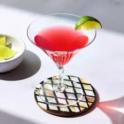Idealny cosmopolitan przepis: orzeźwiający drink z limonką, podany w kieliszku koktajlowym. Obok miseczka z ćwiartkami limonki.