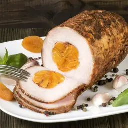 Pyszny schab zawijany z morelami, czosnkiem i bazylią na białym talerzu.