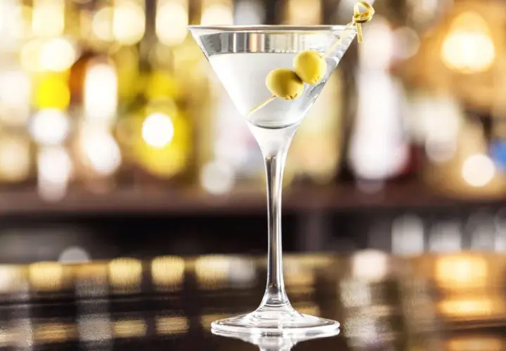 Elegancki drink z martini, ozdobiony dwoma oliwkami na wykałaczce, stoi na błyszczącym blacie.