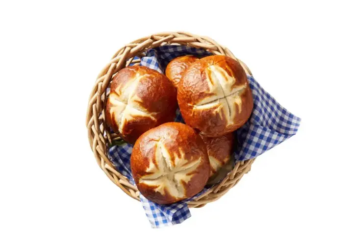 Koszyk z kilkoma świeżymi bułkami bawarskimi, ułożonymi na niebiesko-białej kratkowanej serwetce.