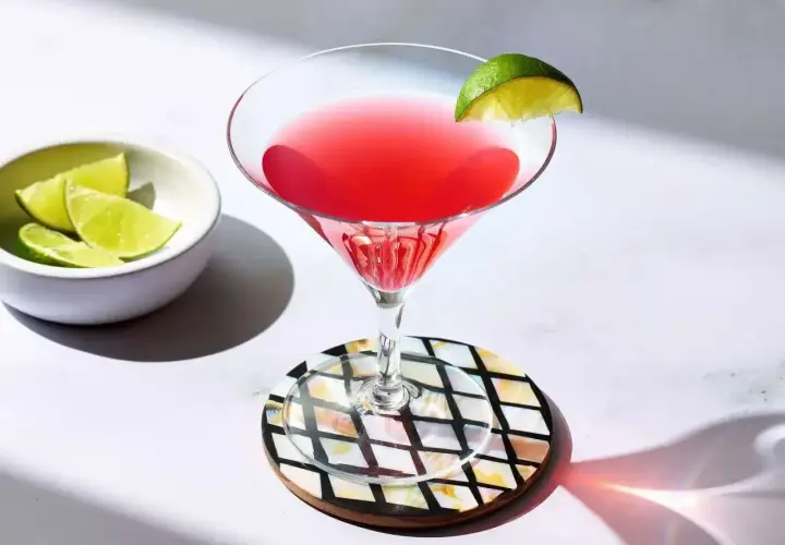 Idealny cosmopolitan przepis: orzeźwiający drink z limonką, podany w kieliszku koktajlowym. Obok miseczka z ćwiartkami limonki.