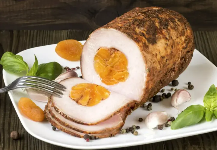 Pyszny schab zawijany z morelami, czosnkiem i bazylią na białym talerzu.