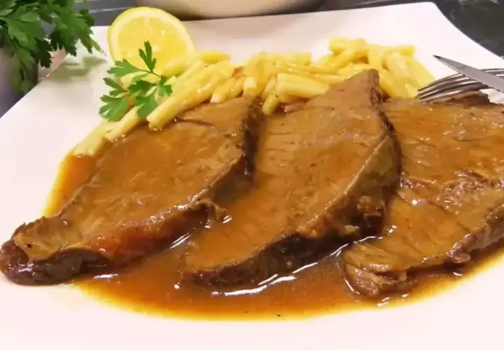 Trzy plastry soczystej łaty wołowej w sosie, podane z makaronem, plasterkiem cytryny i natką pietruszki.