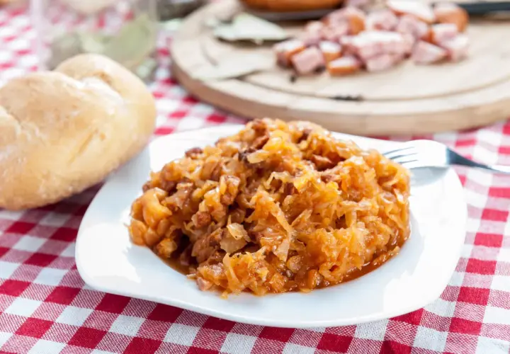Pyszny bigos na talerzu, obok bułka i kiełbasa. Idealne przyprawy do bigosu sprawiają, że danie wygląda apetycznie.