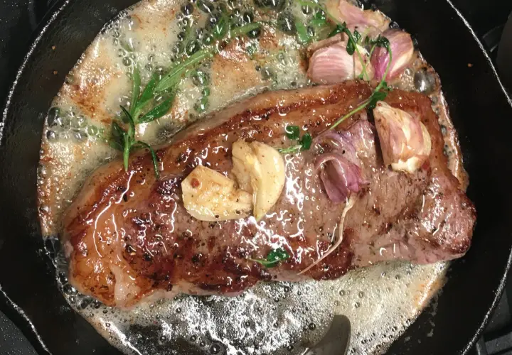 Soczysty rostbef wołowy smaży się na maśle z czosnkiem i rozmarynem w żeliwnej patelni.
