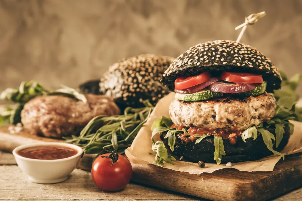 Soczysty burger z czarną bułką, kotletem, warzywami i sosem.