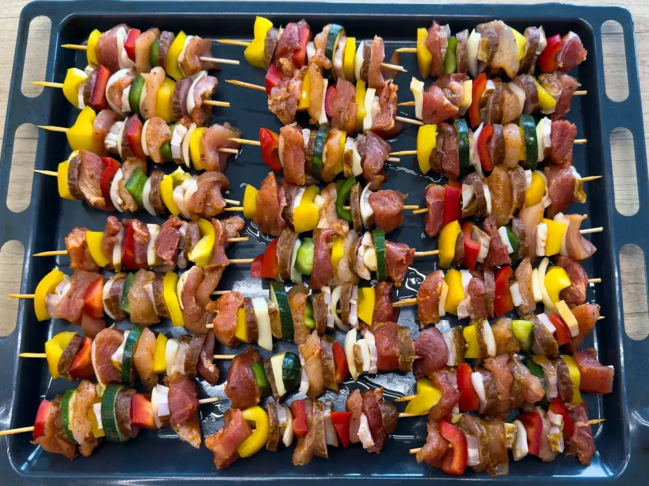 Gotowy przepis na szaszłyki: kawałki mięsa, papryki, cebuli i cukinii ułożone na patyczkach, czekają na grillowanie.